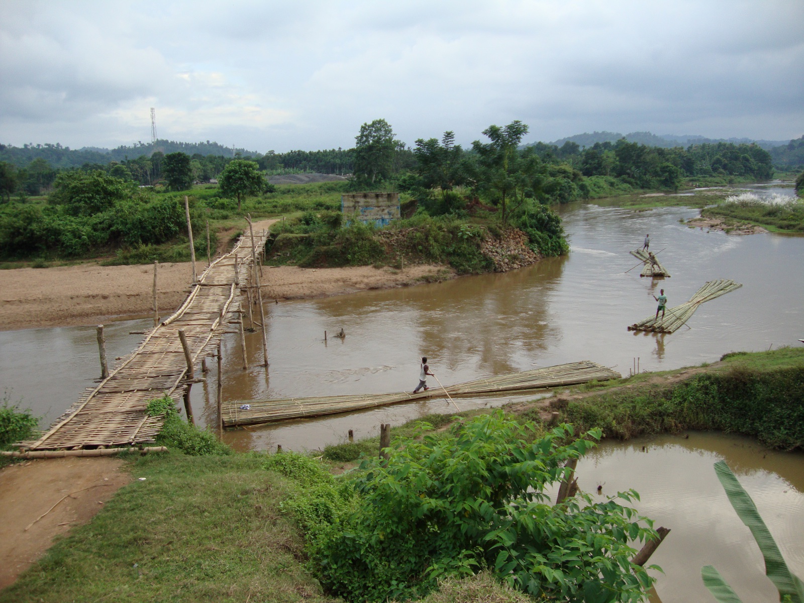 Wooden and bamboo bridge over the Jinari River (left). The bridge is built next to an incomplete concrete bridge (top center). Rafts carry bamboo to market.