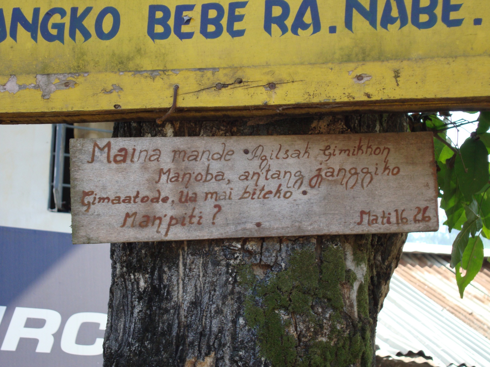 An example of modern written Garo: a Bible verse posted on a tree in Bajengdoba. (The text reads, in KJV: "For what is a man profited, if he shall gain the whole world, and lose his own soul? or what shall a man give in exchange for his soul?" Matthew 16:26.)